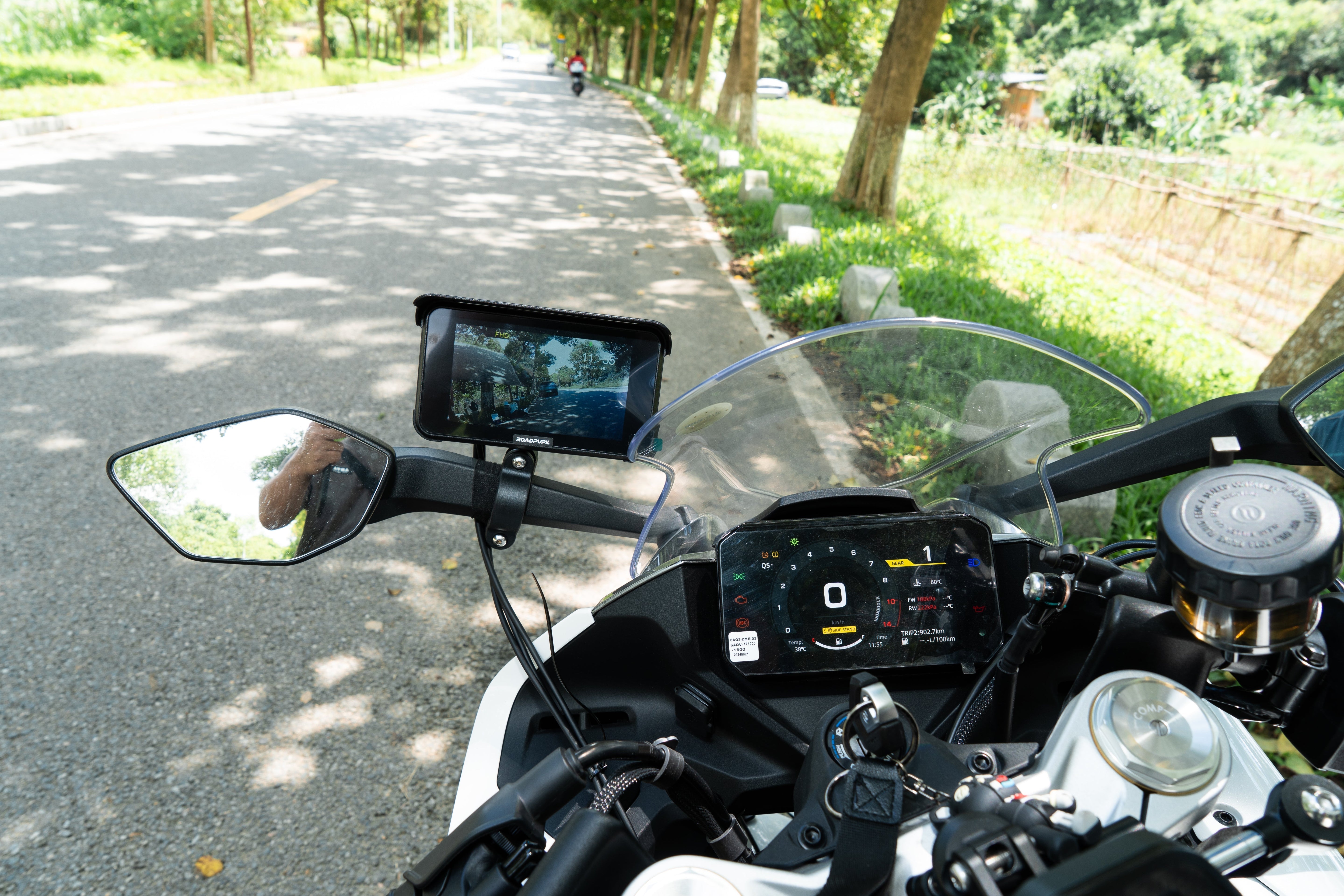 Motorcycle cockpit with a handlebar-mounted wireless CarPlay navigation display on a tree-lined road