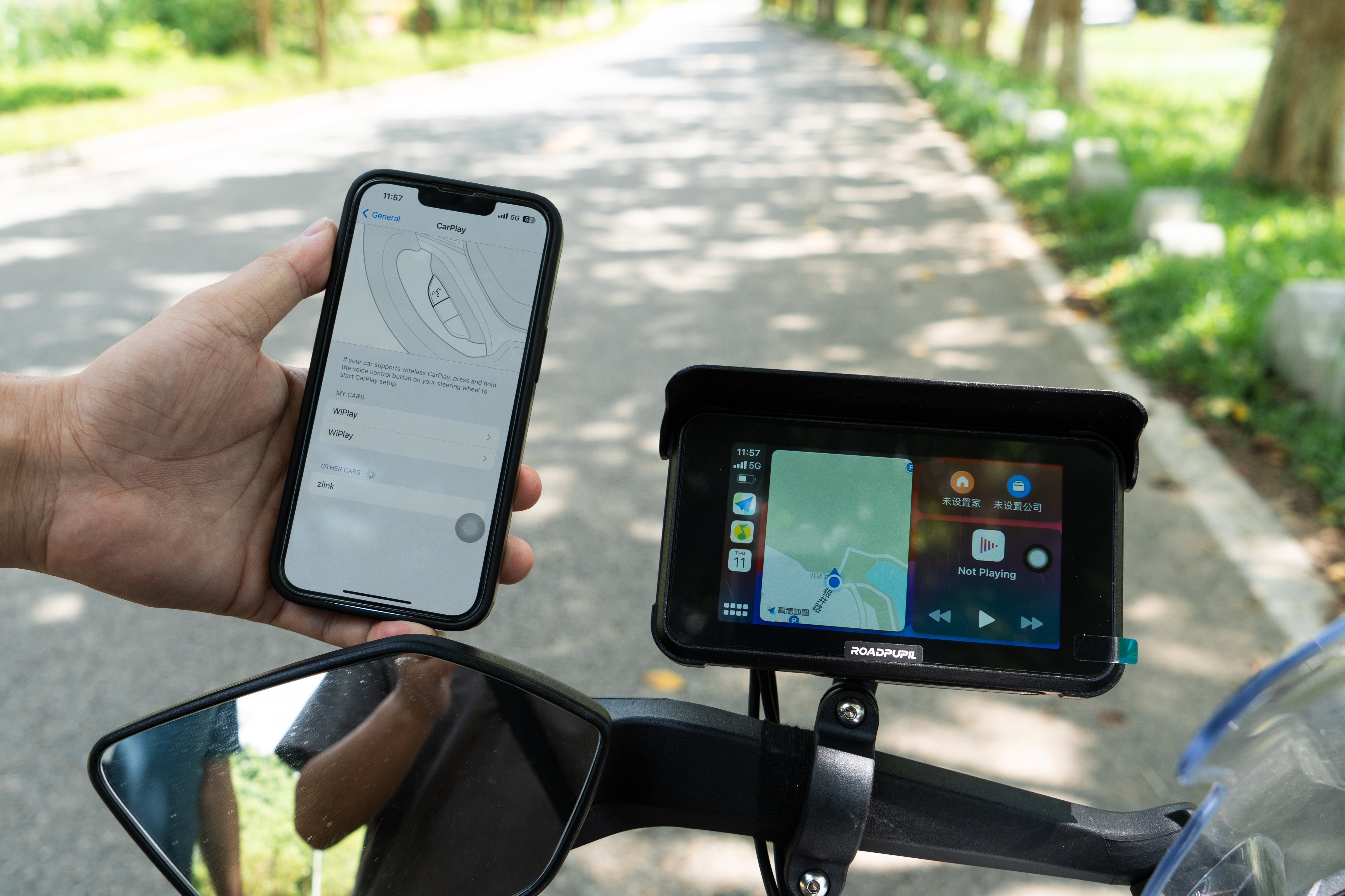 A hand holds a phone showing a motorcycle camera setup, with the camera for motorcycle mounted on the scooter’s handlebars.